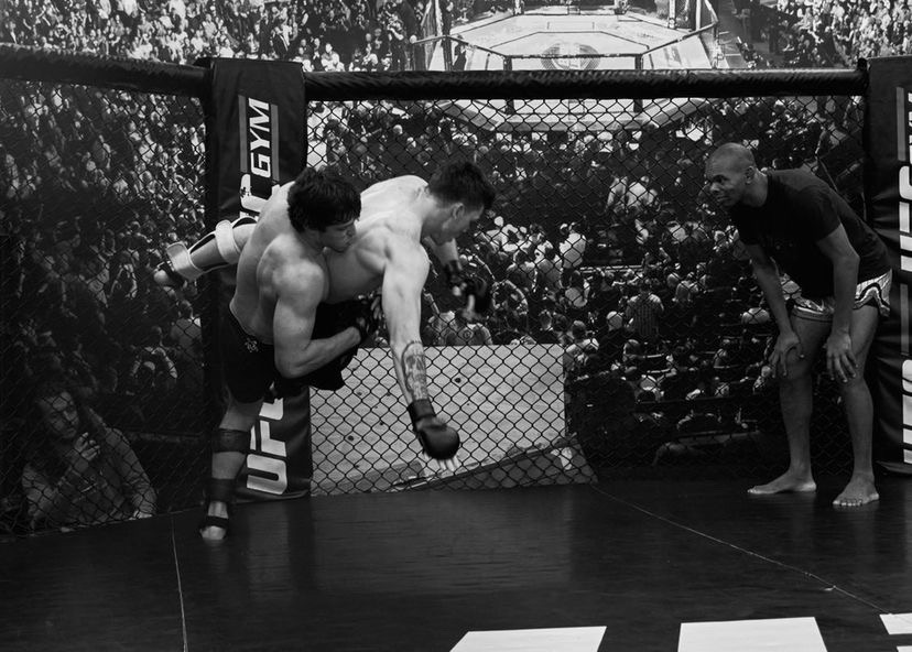 Fabrizio performing a takedown inside an MMA cage, in black and white